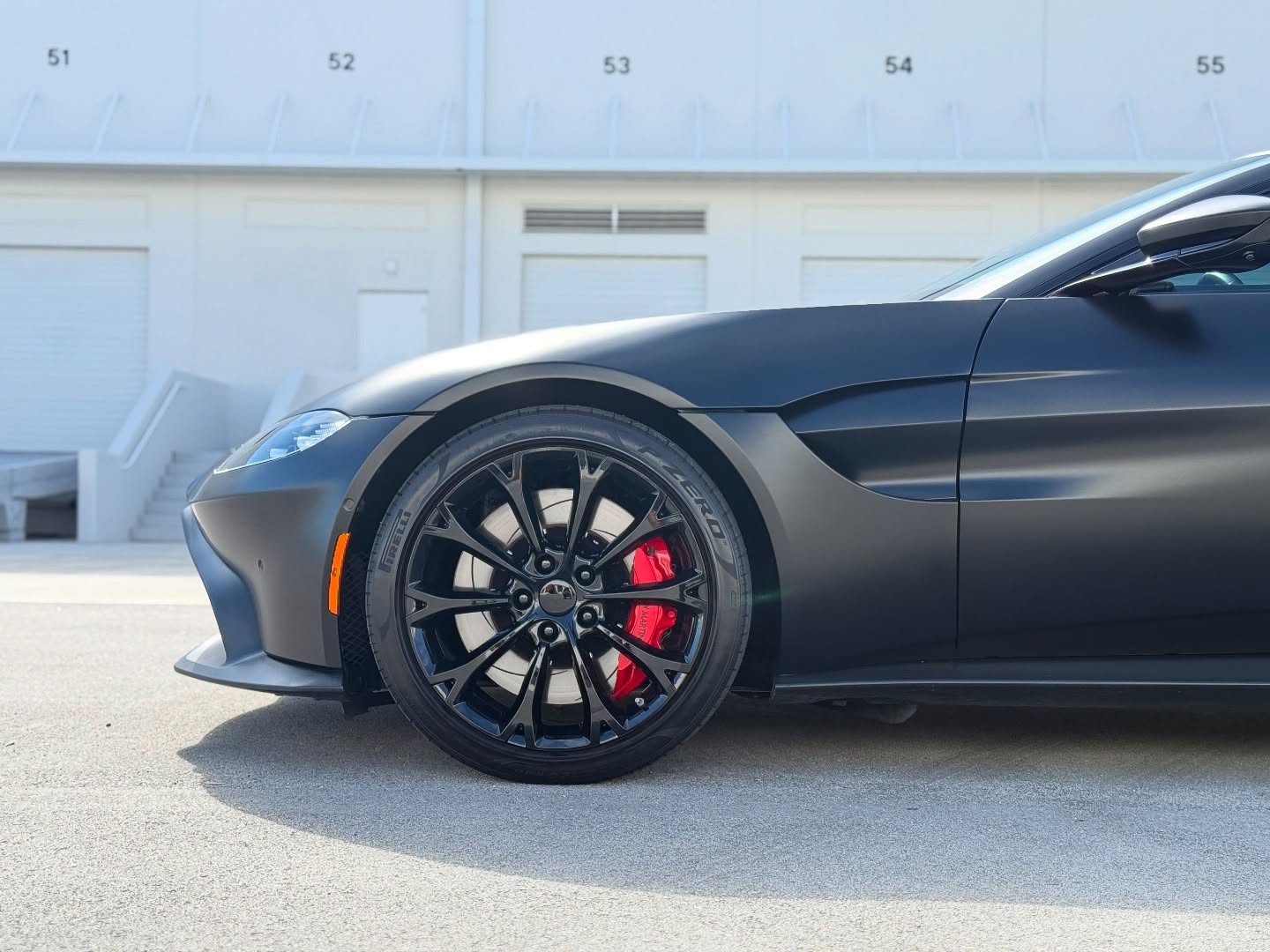 Red brake calipers behind gloss black wheels on a satin black sports car, refinished by Restyle Miami